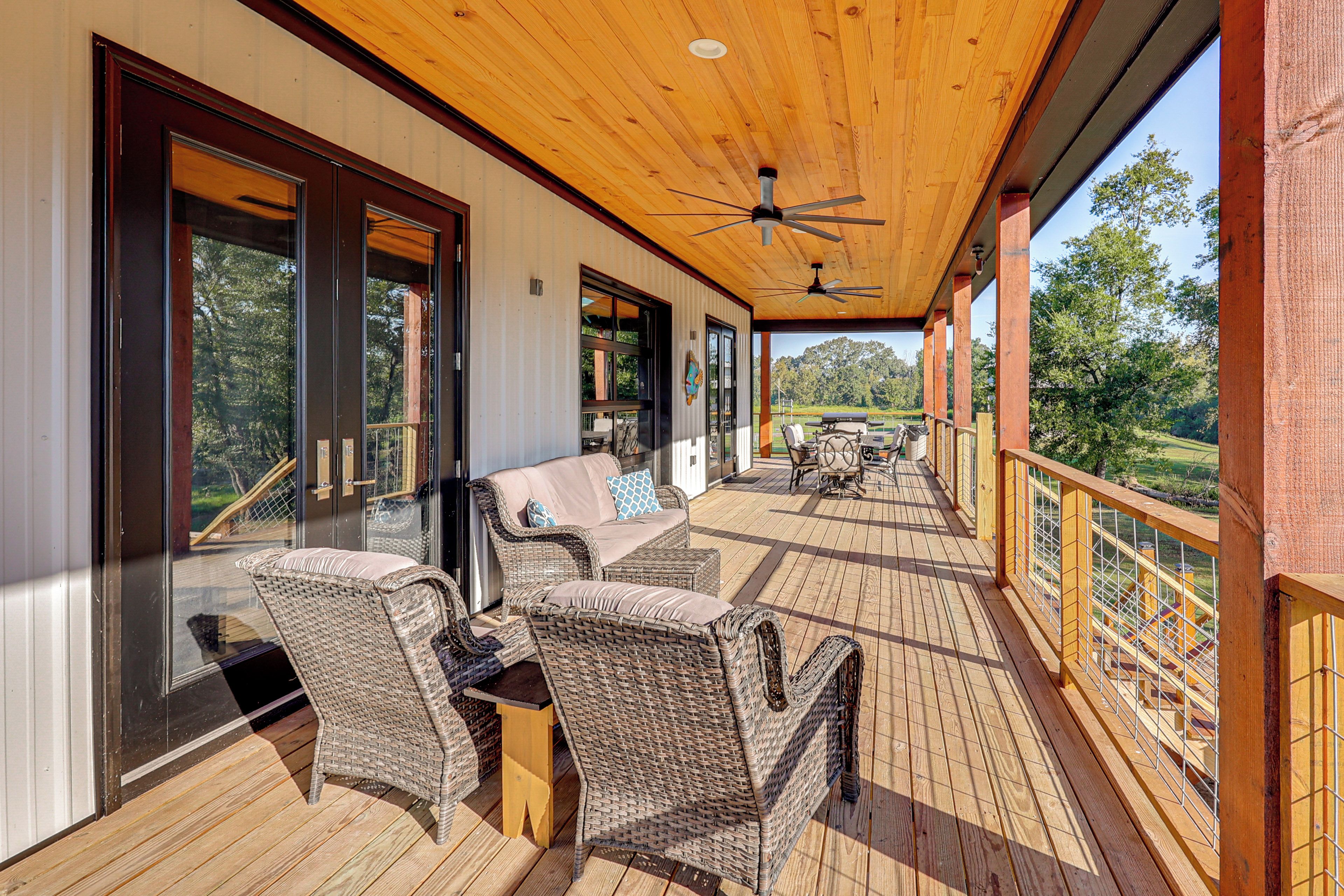 A covered outdoor deck with wicker furniture, a ceiling fan, and a view of the surrounding landscape.