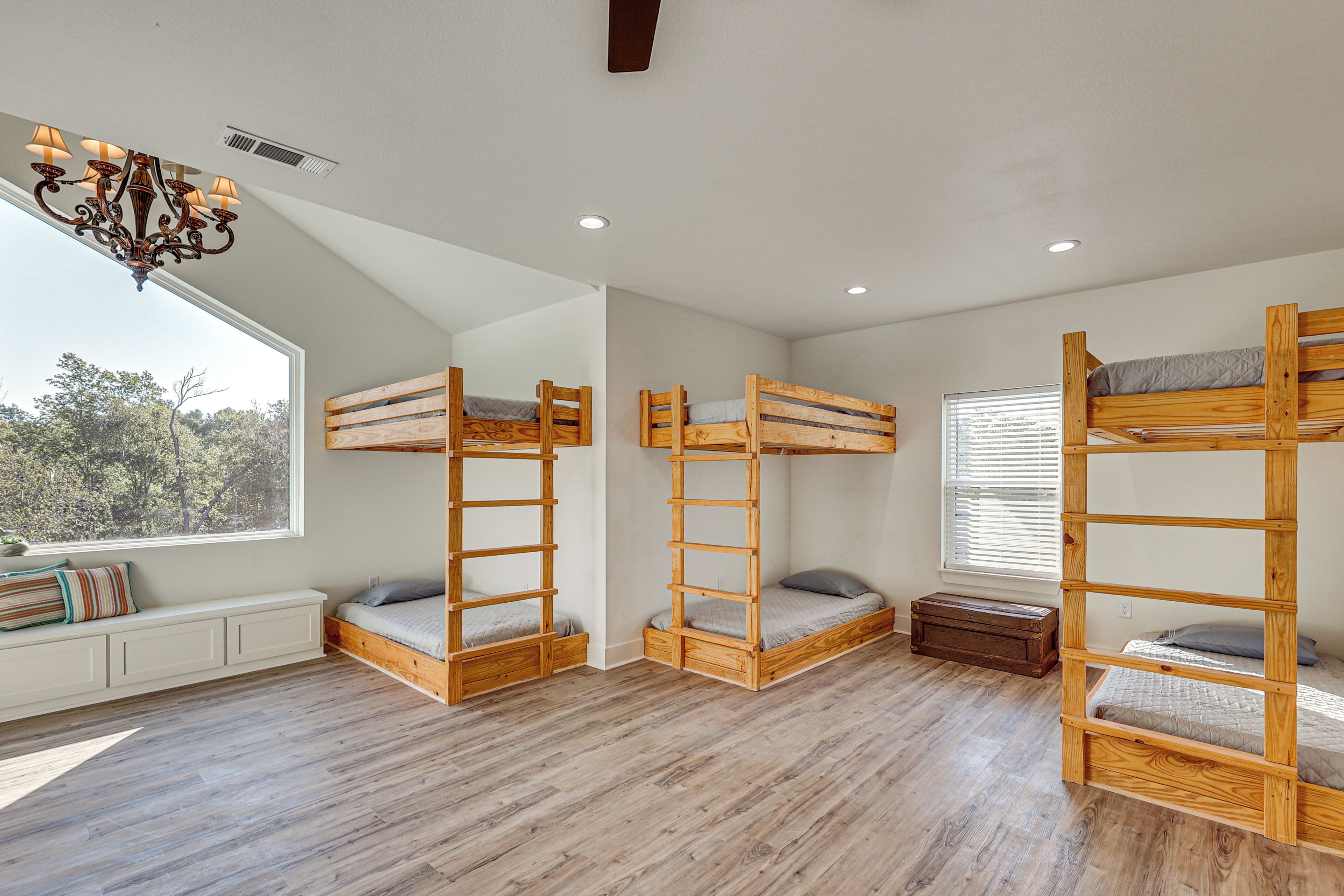 A room with three bunk beds, a window with blinds, a radiator, and a chandelier.