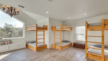 A room with three bunk beds, a window with blinds, a radiator, and a chandelier.