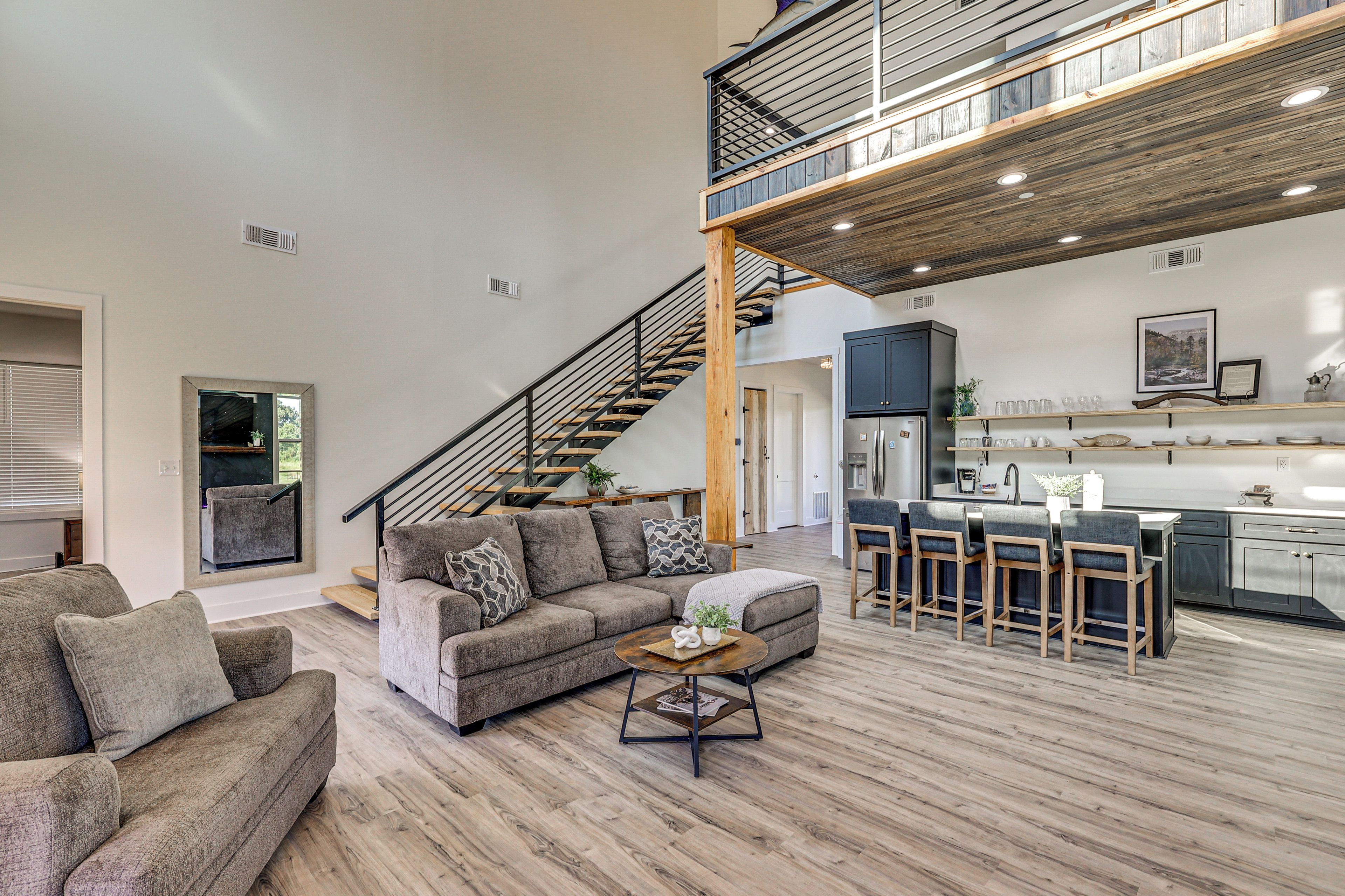 A spacious living area with a high ceiling, a staircase leading to an upper level, and a kitchen with bar seating.