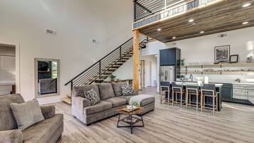 A spacious living area with a high ceiling, a staircase leading to an upper level, and a kitchen with bar seating.