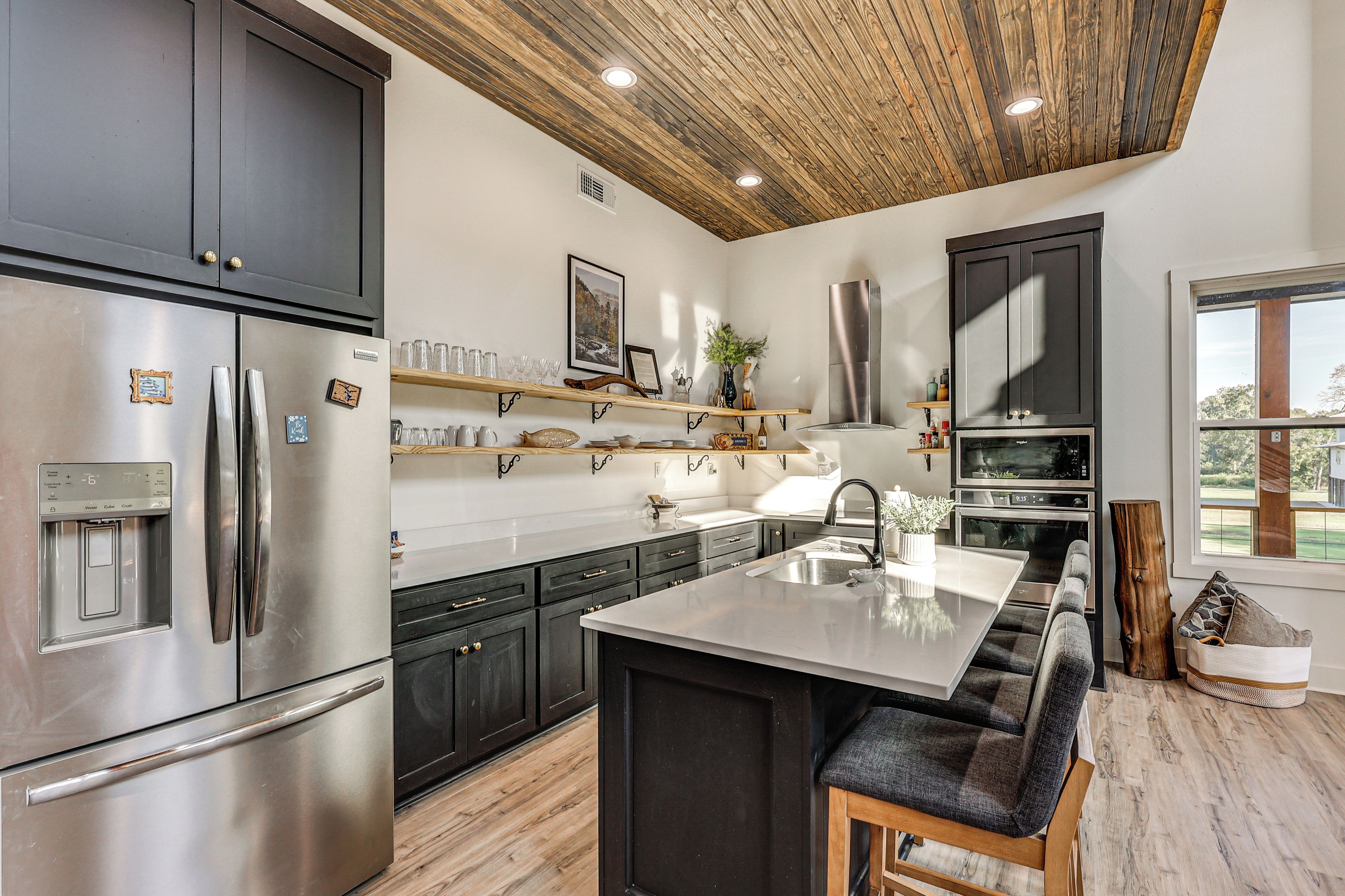 A modern kitchen with a stainless steel refrigerator, a built-in oven, and a wooden ceiling.