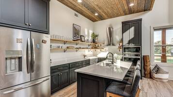 A modern kitchen with a stainless steel refrigerator, a built-in oven, and a wooden ceiling.