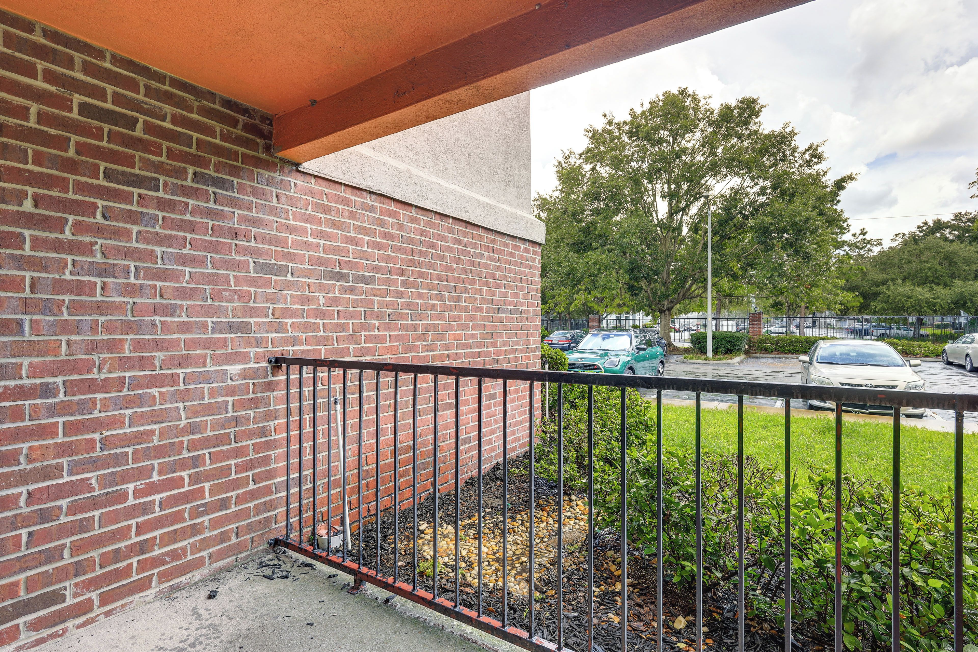 A brick wall with a metal railing, a concrete floor, and a view of parked cars and trees in the background.