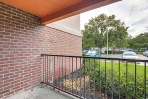 A brick wall with a metal railing, a concrete floor, and a view of parked cars and trees in the background. - Work, Explore & Unwind! Condo 2 Mi to UF (Gainesville)