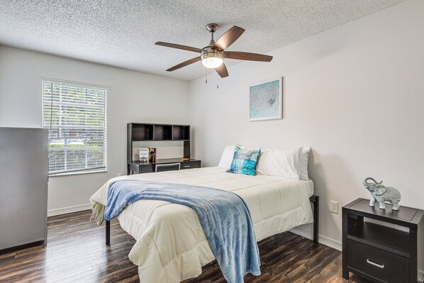 A bedroom with a bed, a desk, a ceiling fan, a window with blinds, and a wall-mounted shelf. - Work, Explore & Unwind! Condo 2 Mi to UF (Gainesville)