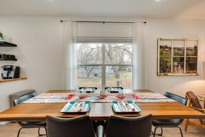 A dining area with a wooden table set for four, a window with a view of trees and a fence, and a shelf with kitchen items. - Spacious Duplex Duo: 14 Mi to Pearl Street Mall (Erie)