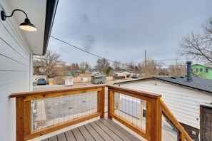 A wooden deck with a metal railing, a hanging light fixture, and a view of a residential area with houses and a parked vehicle. - Spacious Duplex Duo: 14 Mi to Pearl Street Mall (Erie)