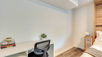 A bedroom with a wooden headboard, a white desk with a chair, a small plant, and a bedside table with a tissue box.