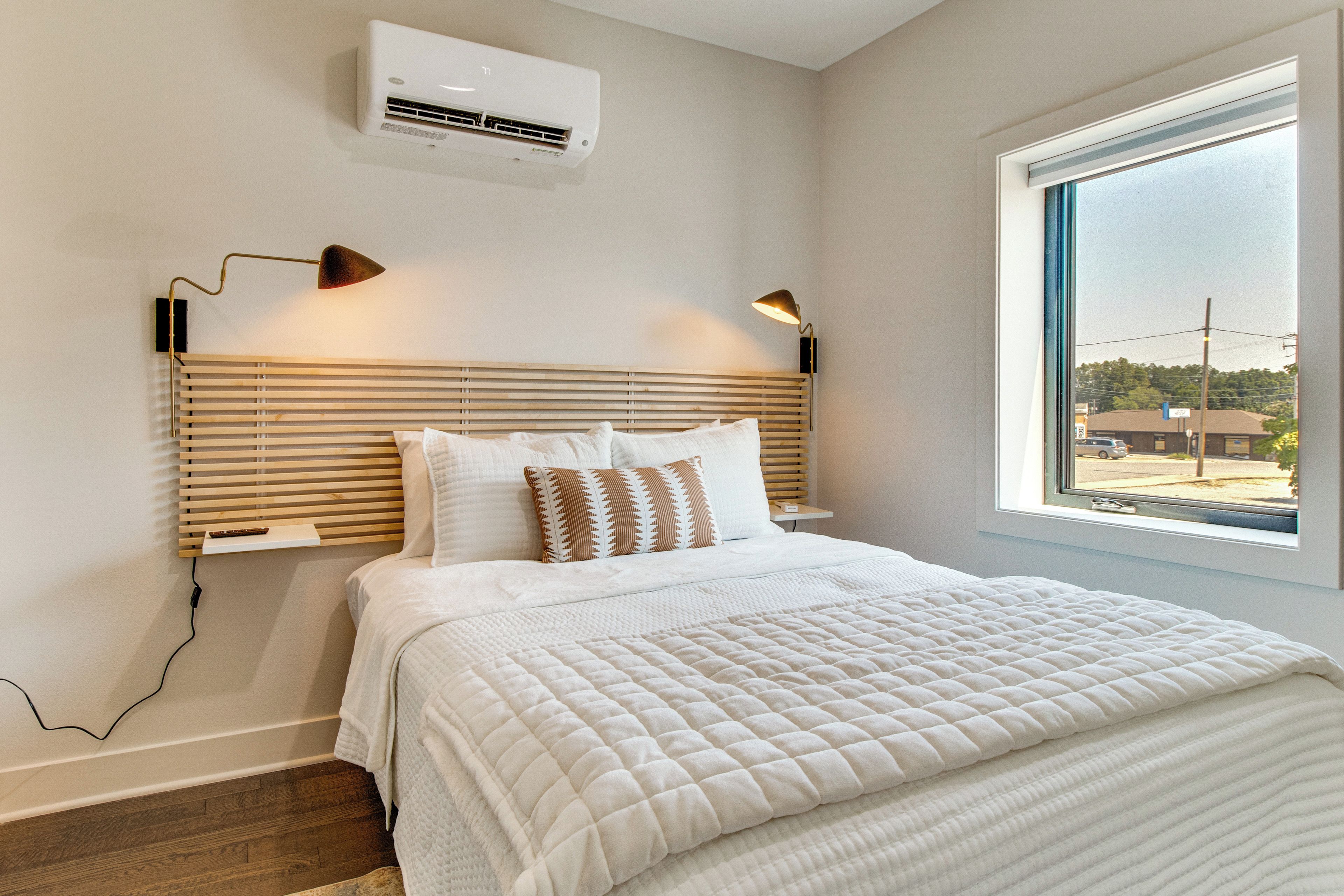 Un dormitorio con cama, lámparas de noche, aire acondicionado y una ventana con vistas.