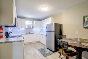 Uma cozinha compacta com armários brancos, geladeira de aço inoxidável e um espaço de refeições com mesa e cadeiras de madeira.