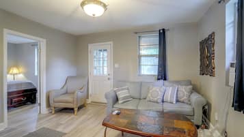 Una sala de estar con sofá, sillón, mesa de centro y una puerta que da a otra habitación.