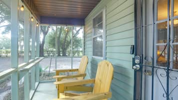 A porch with two wooden Adirondack chairs, a metal gate, and a view of trees.