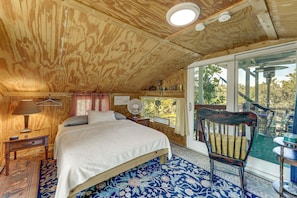 Un dormitorio con techo de madera, una cama, una silla, un ventanal y vistas al exterior.