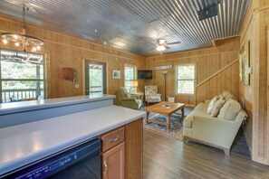 A cabin interior with a kitchen area, a dining table, a sofa, and a ceiling fan. - Deep-water Lake Sinclair Escape in Quiet Cove (Milledgeville)