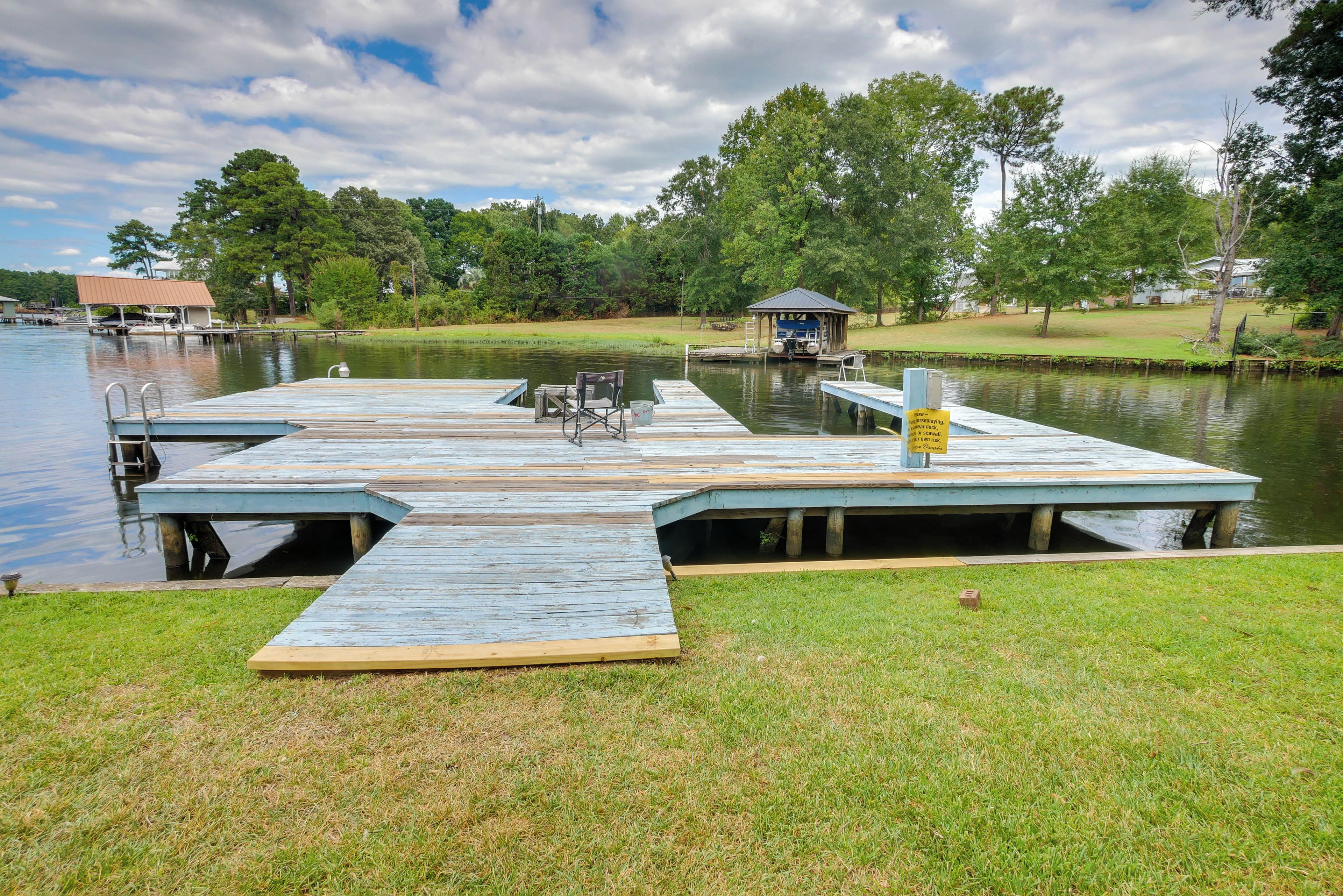 A wooden dock extending into a calm lake, with a small pavilion and a grassy area in the foreground.