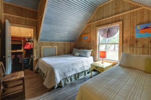 A bedroom with a sloped ceiling, a bed, a nightstand, a window with a view of trees, and a closet with hanging clothes. - Deep-water Lake Sinclair Escape in Quiet Cove (Milledgeville)