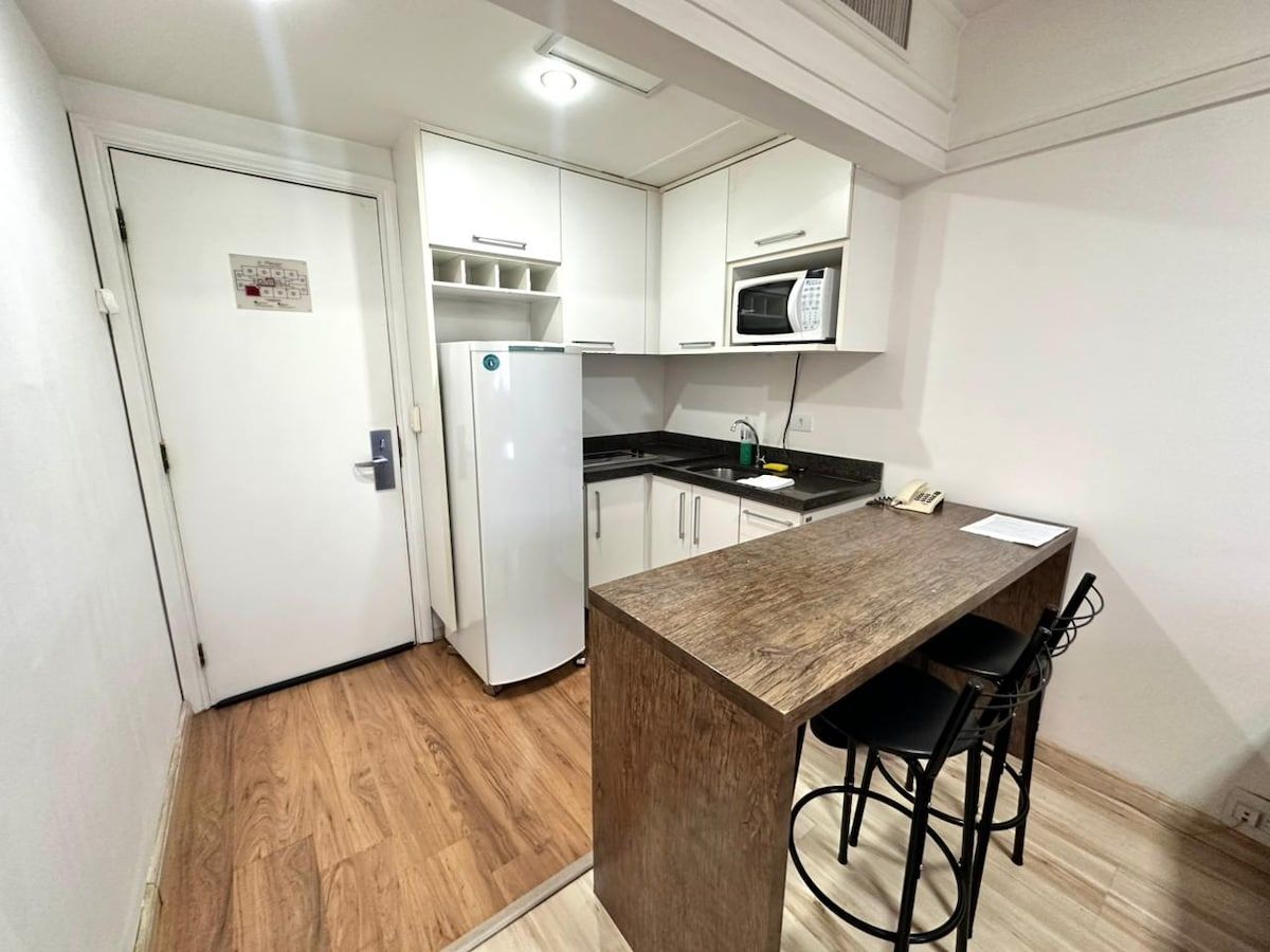 Eine kompakte Küche mit weißen Schränken, einer Mikrowelle, einem Kühlschrank und einer Holz-Kochinsel mit zwei Barhocker.