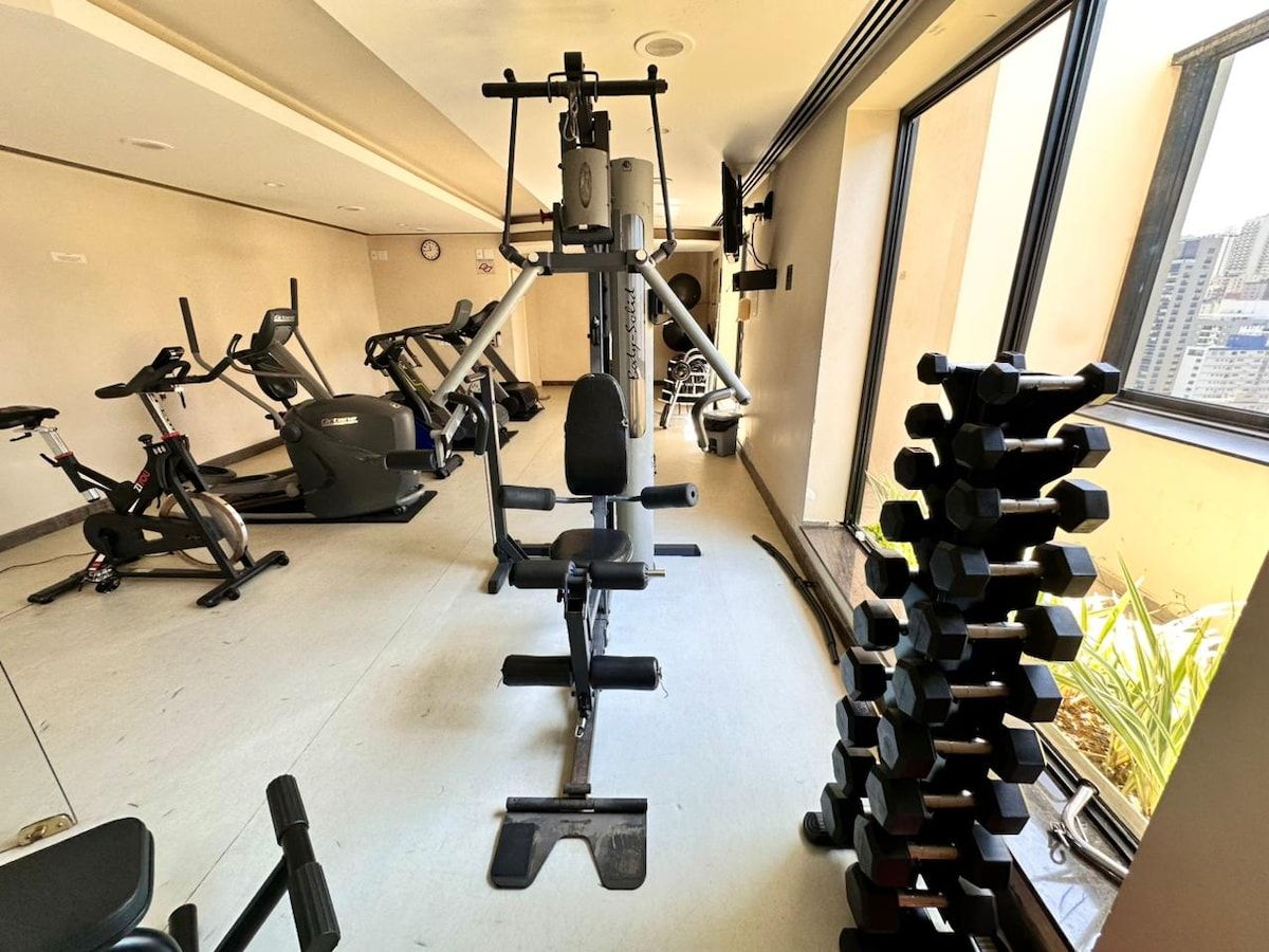 Ein Fitnessstudio mit verschiedenen Trainingsgeräten, darunter Laufbänder, eine Bankpresse und Kurzhanteln.