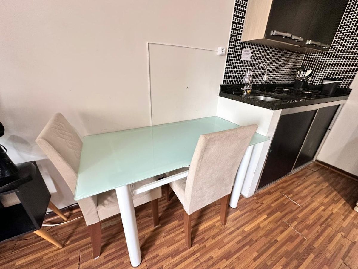 A small kitchenette with a black countertop, a white cabinet, and a glass table with a chair.