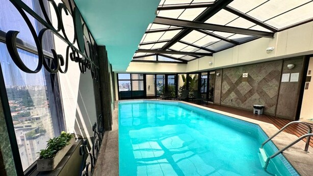 An indoor swimming pool with a view of the cityscape through large windows. - Le Premier Suites (São Paulo)