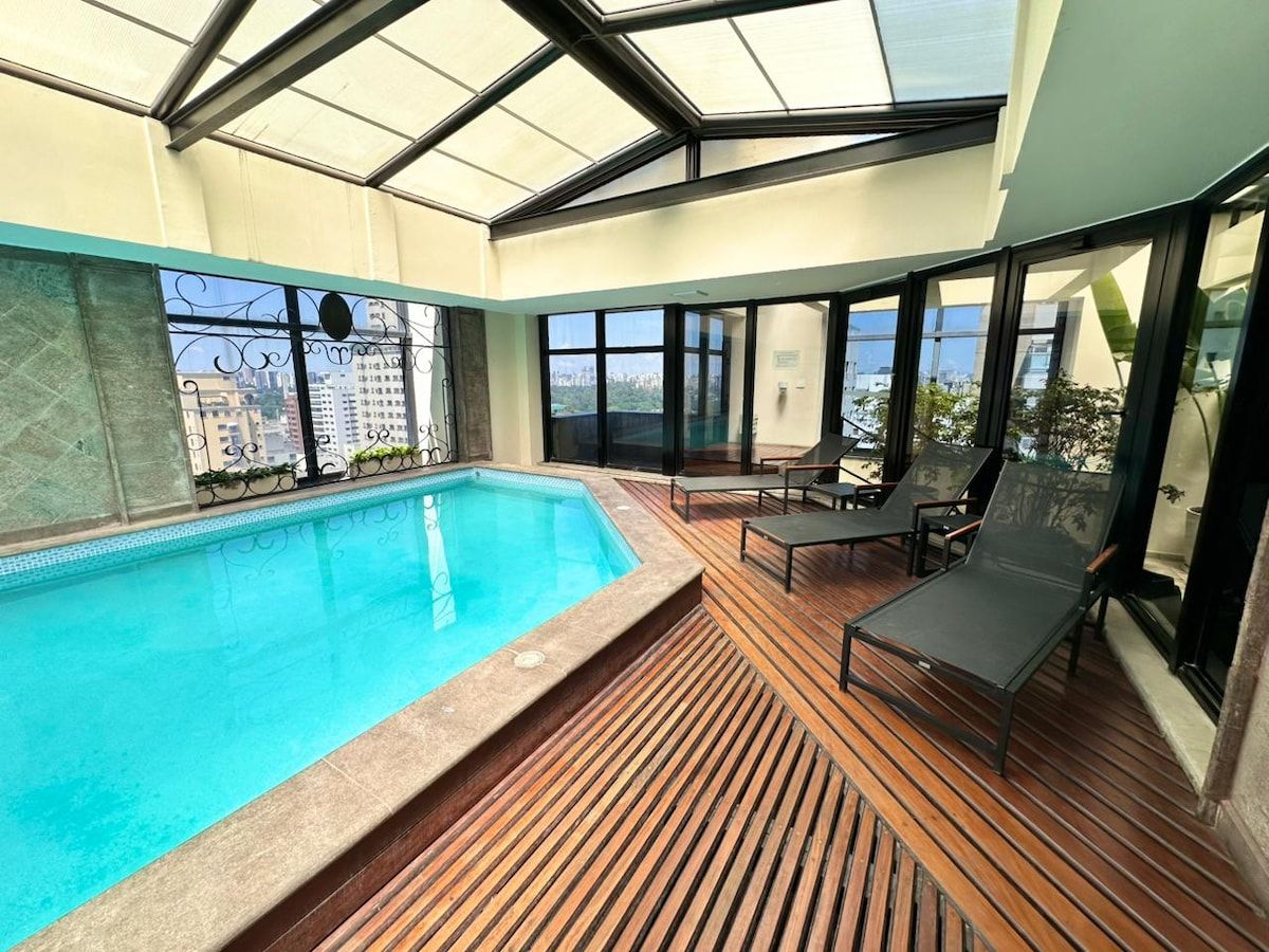 A rooftop swimming pool with a wooden deck and lounge chairs.