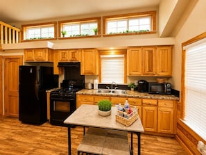 A kitchen with wooden cabinets, a black refrigerator, a stove, a microwave, and a table with a basket and a plant. - Lake Travis Cabin Family Fun Resort Pool & Hot Tub (Austin)