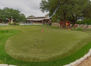 Um campo de golfe bem cuidado com um putting green, um clube de campo ao fundo e um muro de pedra.