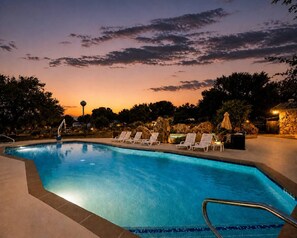A swimming pool with lounge chairs and a stone wall in the background. - Lake Travis Cabin Family Fun Resort Pool & Hot Tub (Austin)