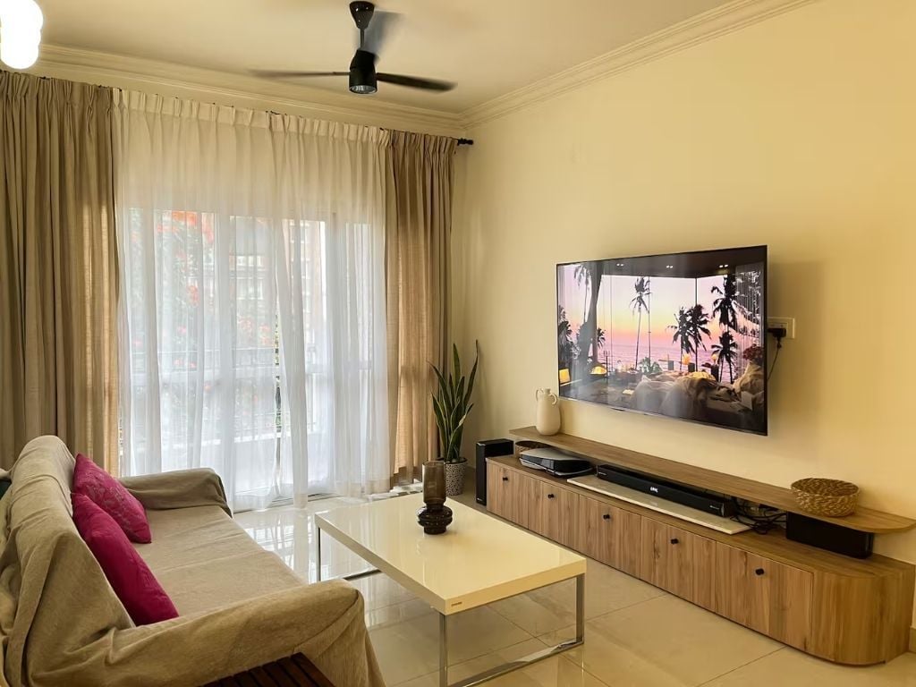 Un salon comprenant un canapé, une table basse, un téléviseur à écran plat fixé au mur et un ventilateur de plafond.