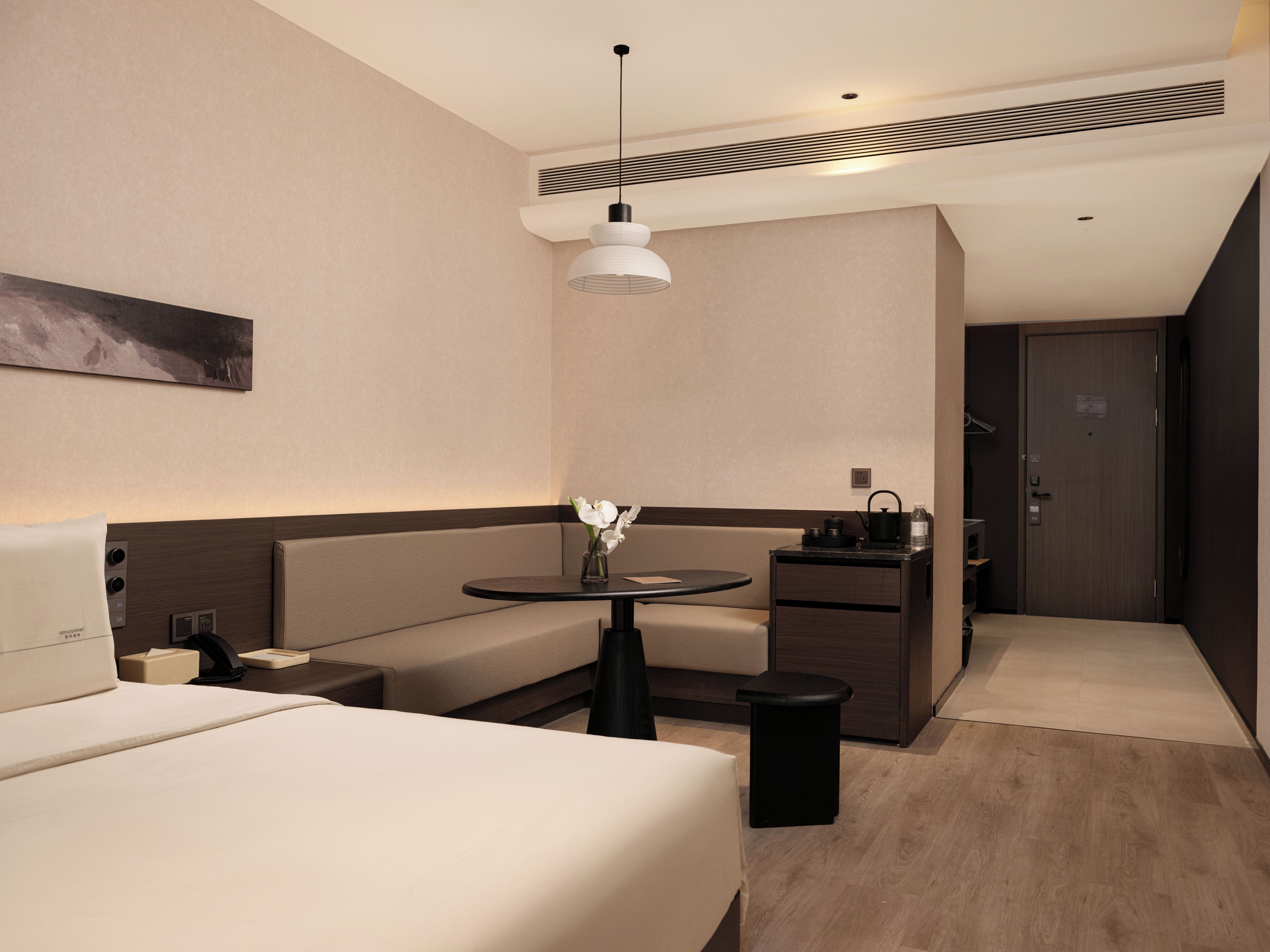 Una habitación de hotel moderna con cama, zona de estar, una mesita con un florero, kitchenette y una puerta.