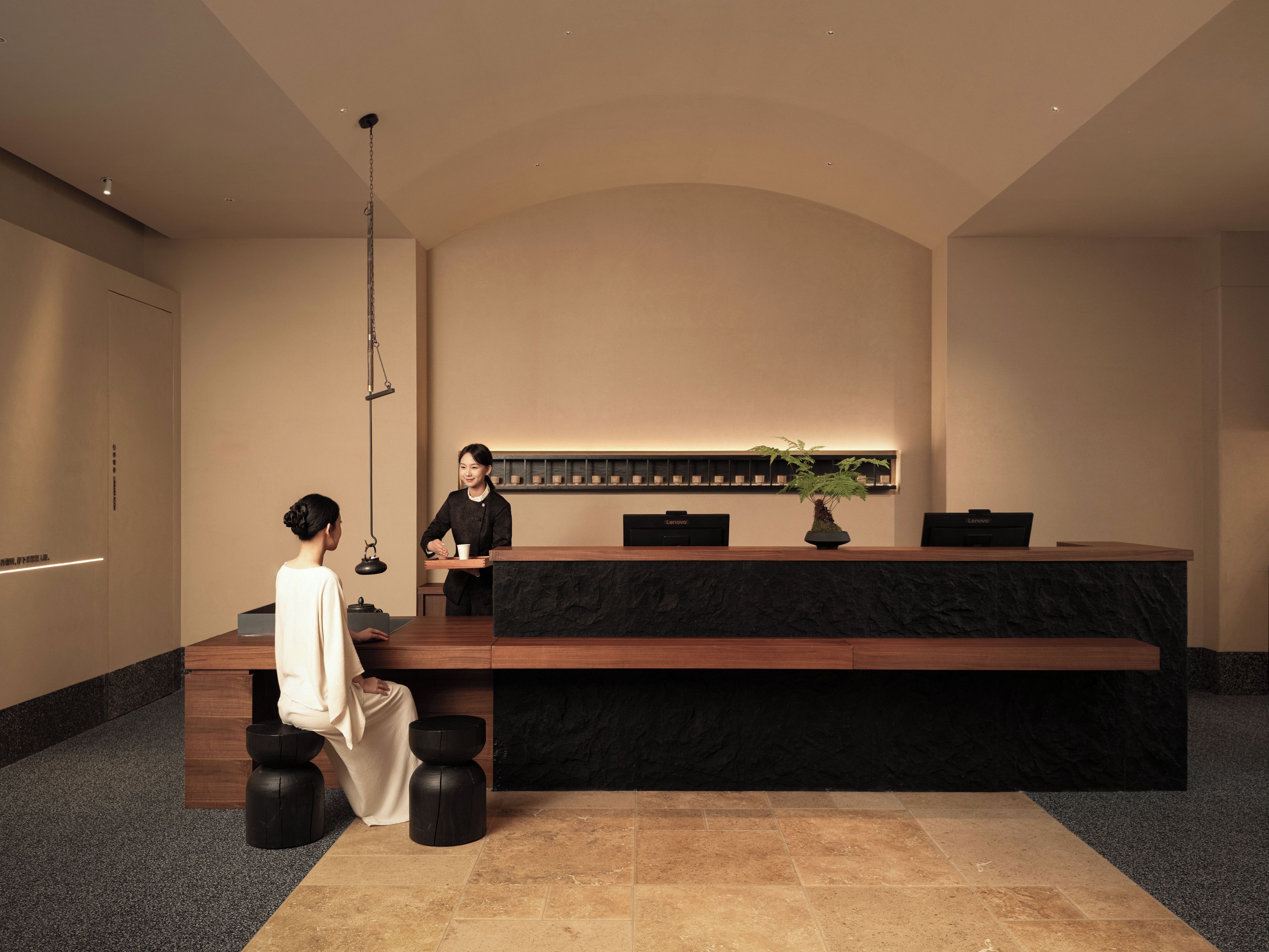 A reception desk with a black marble top, a potted plant, and a wall-mounted display.