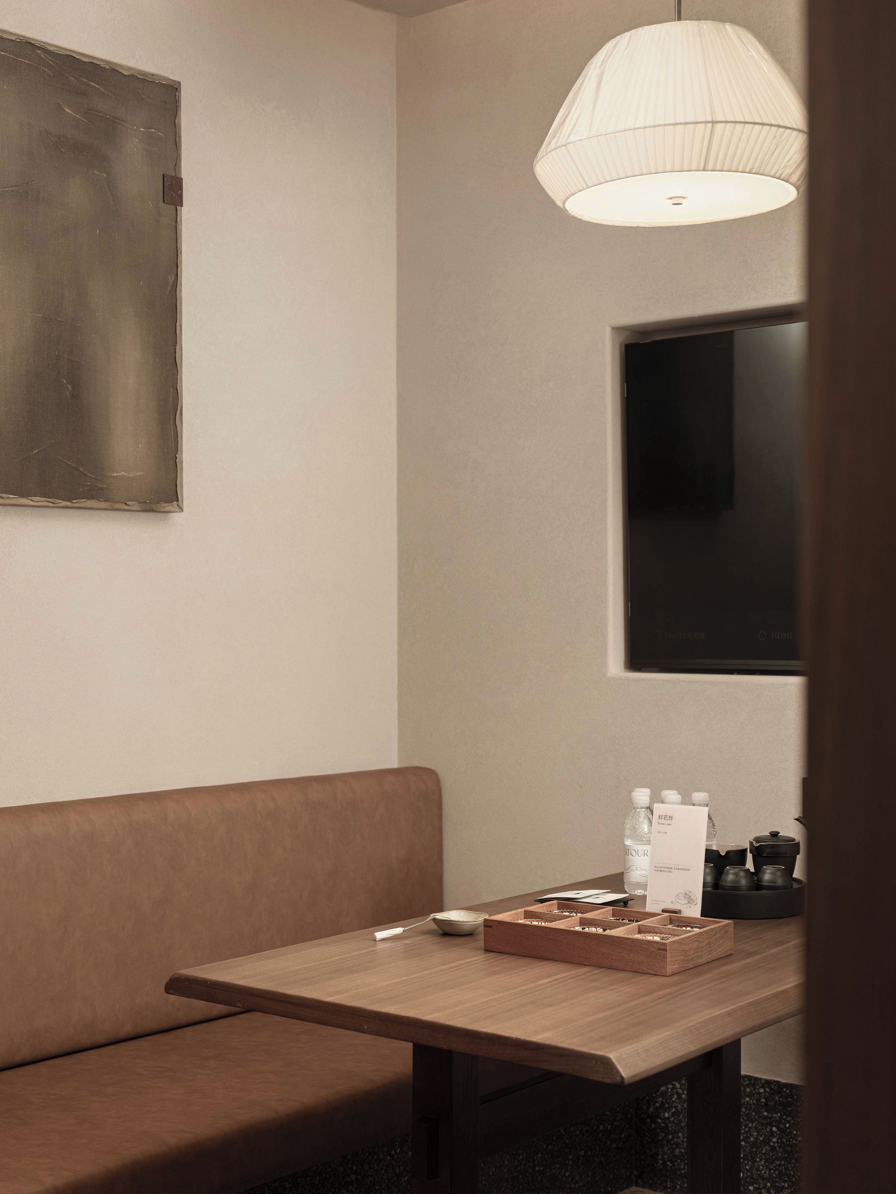 Une pièce avec une table en bois, un canapé marron, un téléviseur fixé au mur et un luminaire suspendu.