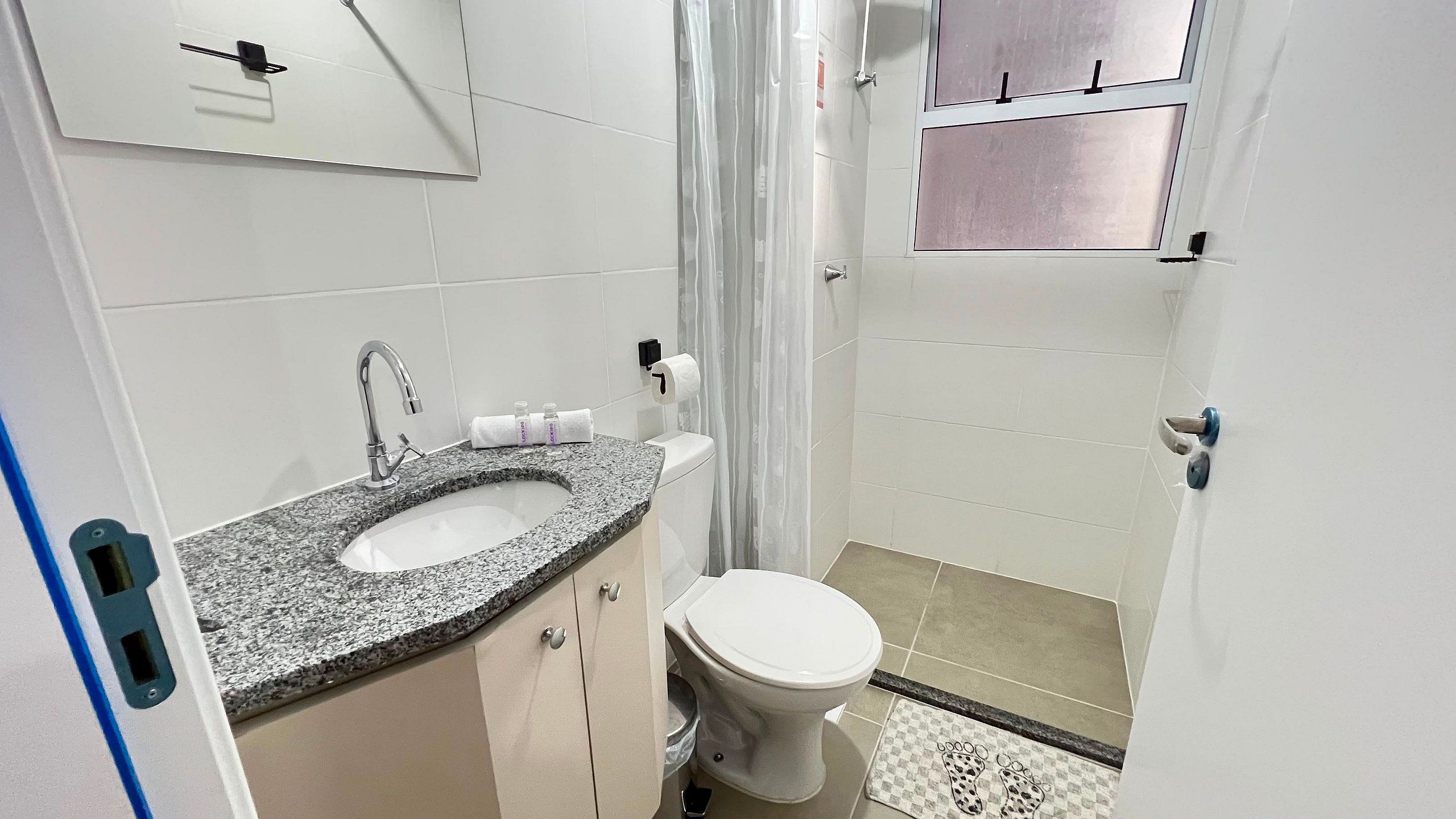 Een kleine badkamer met een wastafel met een granieten blad, een wit toilet en een douchehoek.
