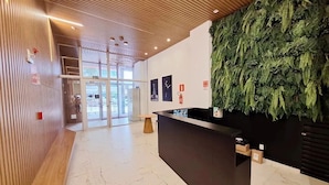Zona de recepción con techo de madera, un mostrador de recepción y una pared decorada con una instalación de hojas verdes.