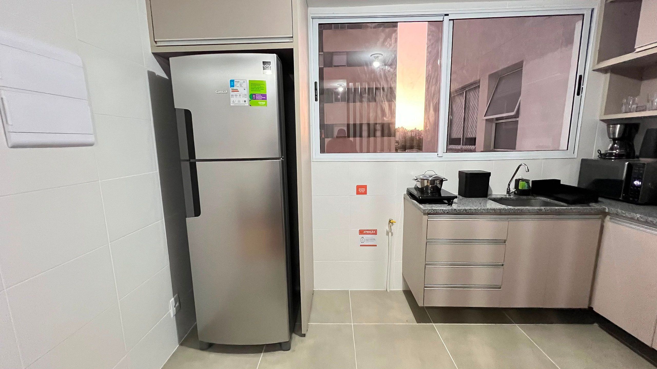 Una cocina compacta con refrigerador, lavamanos y ventana.