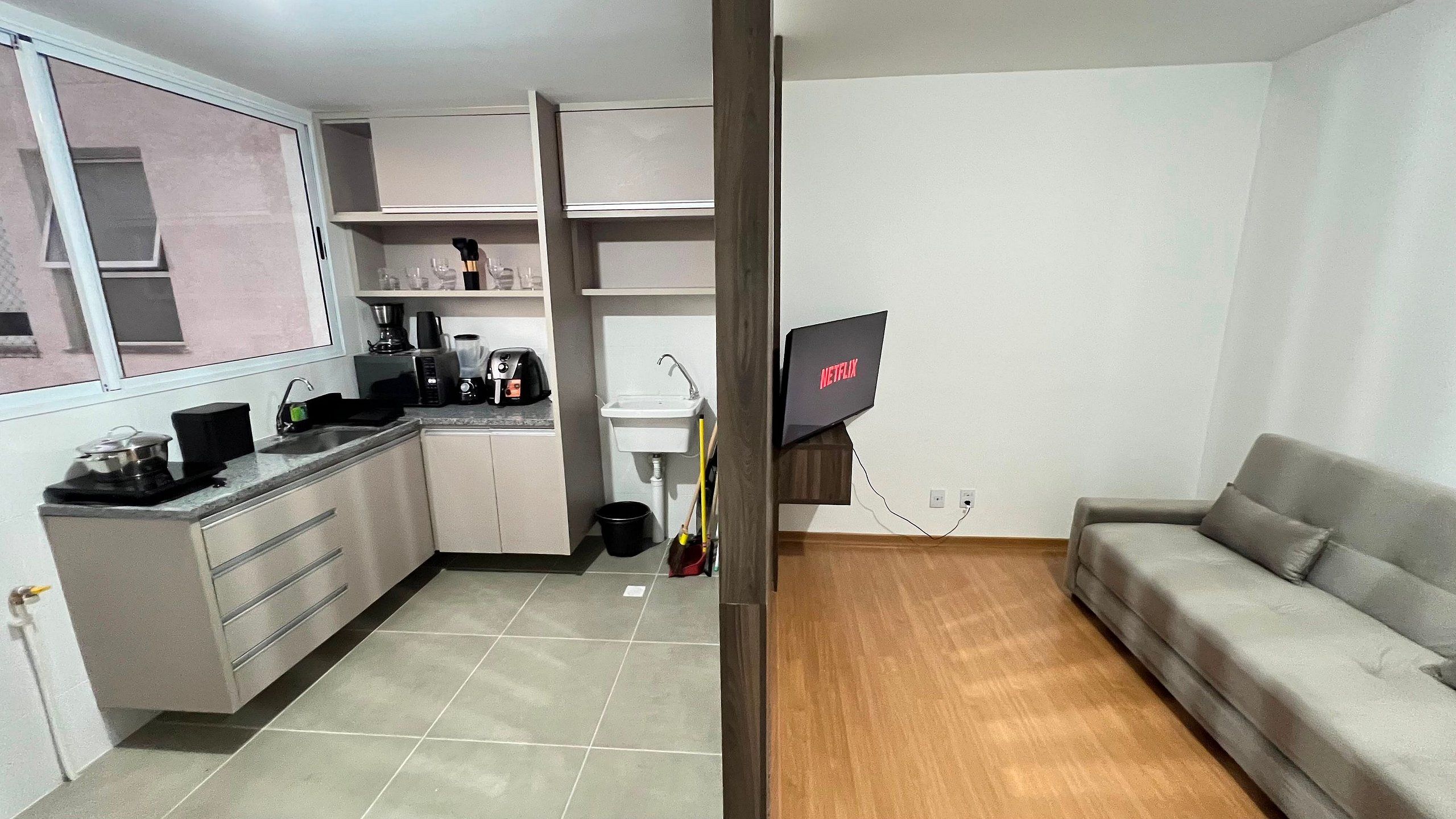 Un espacio habitable compacto con kitchenette, un sofá y un televisor de pantalla plana montado en la pared.
