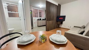 Una mesa de comedor con platos y vasos, un televisor montado en la pared y un sofá en la sala.