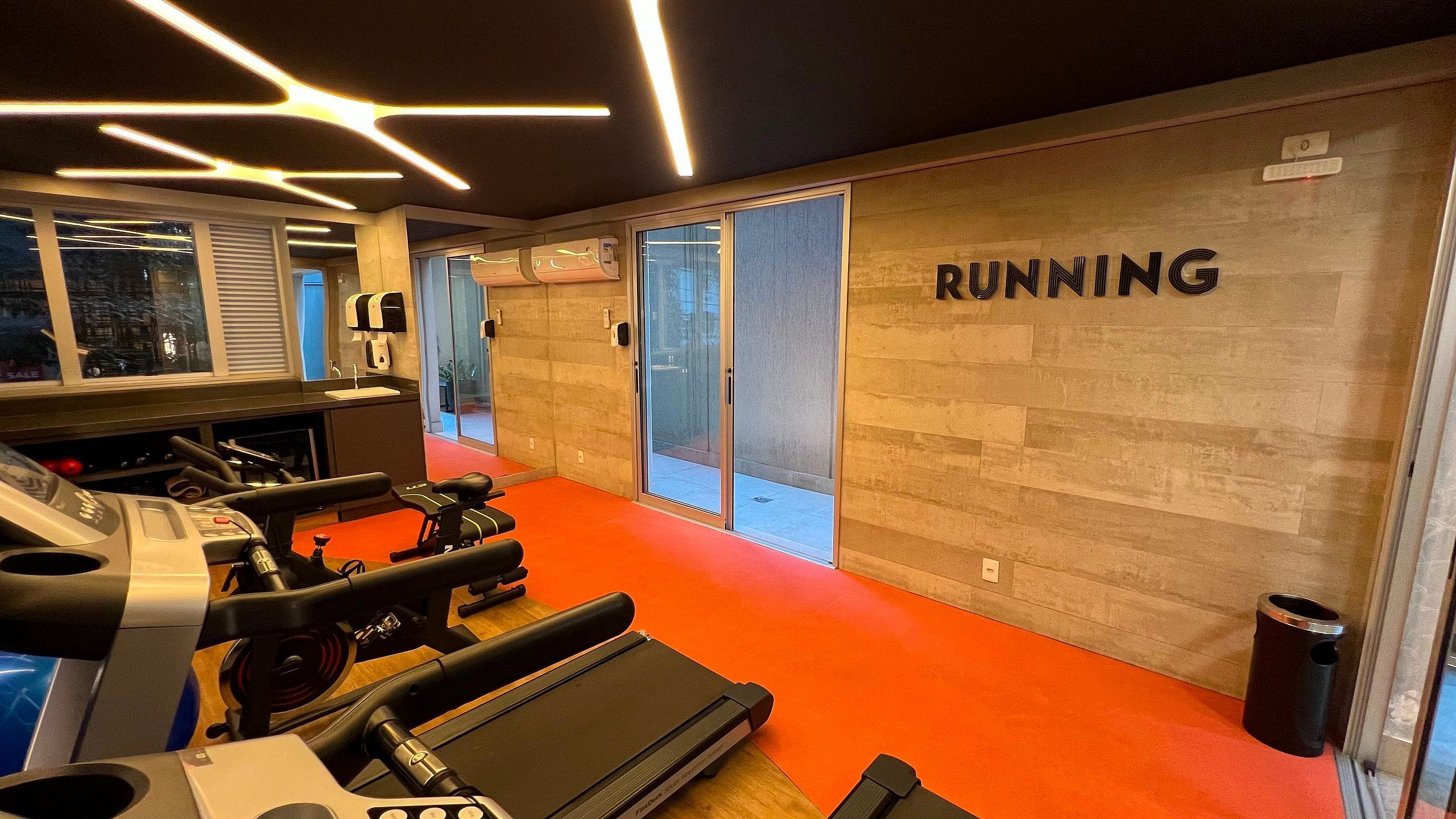 Un gimnasio con equipo de ejercicio, una alfombra roja y una pared con la palabra 'RUNNING'.