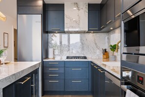 A modern kitchen with dark cabinetry, marble countertops, and stainless steel appliances. - The Oak Haven | 2BR+2BA | Central | Pool&Sauna (Kelowna)