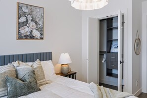 A bedroom with a bed, pillows, a bedside lamp, a wardrobe, and a floral painting on the wall. - The Oak Haven | 2BR+2BA | Central | Pool&Sauna (Kelowna)
