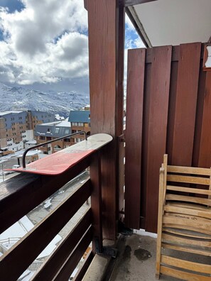 A balcony with a wooden railing, a red snowboard leaning against it, and a wooden chair. - "V22" by Versant Collection (Val Thorens)