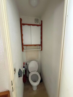 A narrow bathroom with a toilet, a small shelf above the toilet, and a wall-mounted vent. - "V22" by Versant Collection (Val Thorens)