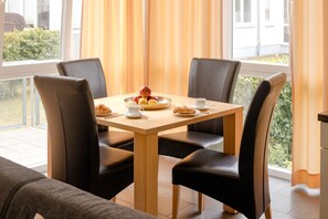 A dining area with a table set for two, featuring a bowl of fruit, croissants, and a cup. - Seestern 32, a family-friendly vacation rental in Großenbrode. An inviting patio with comfortable patio furniture. Wellness oasis with a sauna and hot tub. Storage space for bicycles & seasonal beach chair included (Großenbrode)