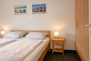 A hotel room with two beds, a wooden headboard, bedside tables with lamps, and two wall art pieces. - Seestern 32, a family-friendly vacation rental in Großenbrode. An inviting patio with comfortable patio furniture. Wellness oasis with a sauna and hot tub. Storage space for bicycles & seasonal beach chair included (Großenbrode)