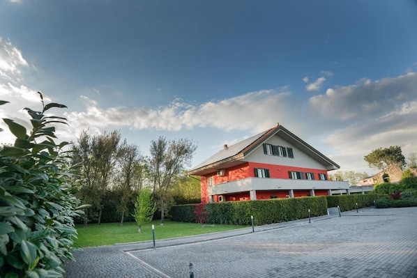 A two-story building with a red and white facade, surrounded by a paved courtyard and greenery.