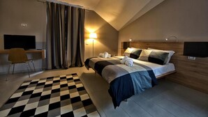 A hotel room with a bed, a desk, a chair, a lamp, and a television. - Lepini Suites Guesthouse (Patrica)