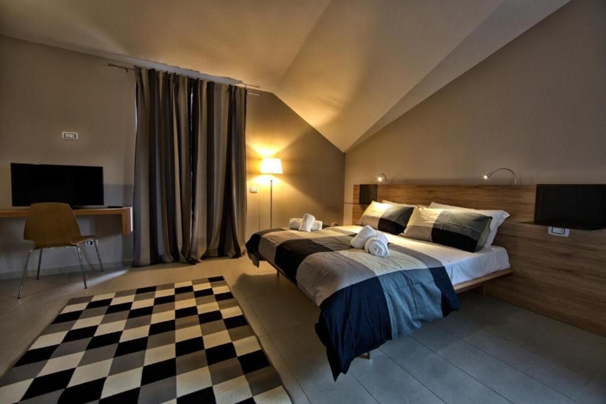 A hotel room with a bed, a desk, a chair, a lamp, and a television.