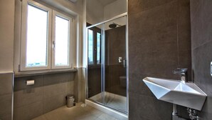 A modern bathroom with a glass-enclosed shower, a white sink, and a window providing natural light. - Lepini Suites Guesthouse (Patrica)