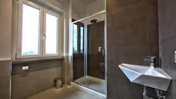 Un baño moderno con ducha envuelta en vidrio, lavamanos blanco y ventana que proporciona luz natural.